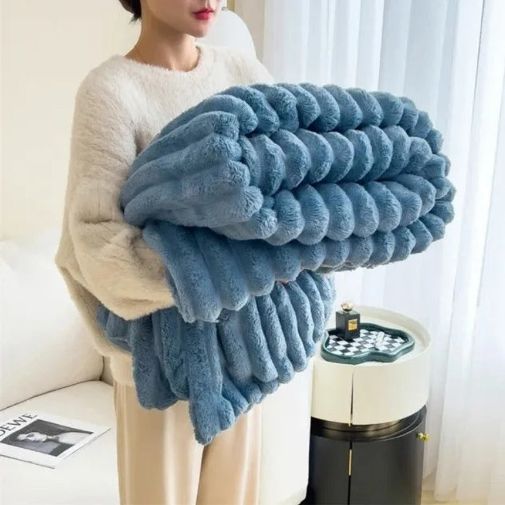 Person holding a large blue textured blanket in a living room setting.