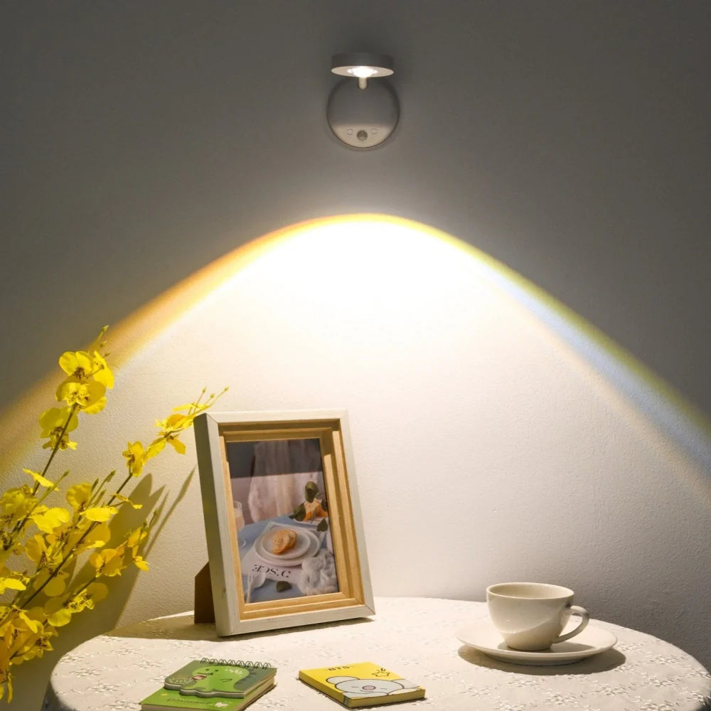 Decorative setup with a framed photo, cup, and flowers on a table under a wall-mounted light fixture.
