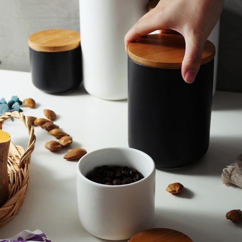 Person opening a black container with a wooden lid on a table with coffee beans and nuts.