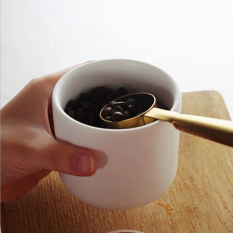 White mug with gold spoon holding coffee beans on a wooden surface