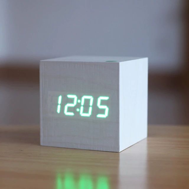 White digital clock with green LED display on a wooden surface