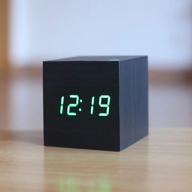 Black digital clock with green LED display on a wooden surface