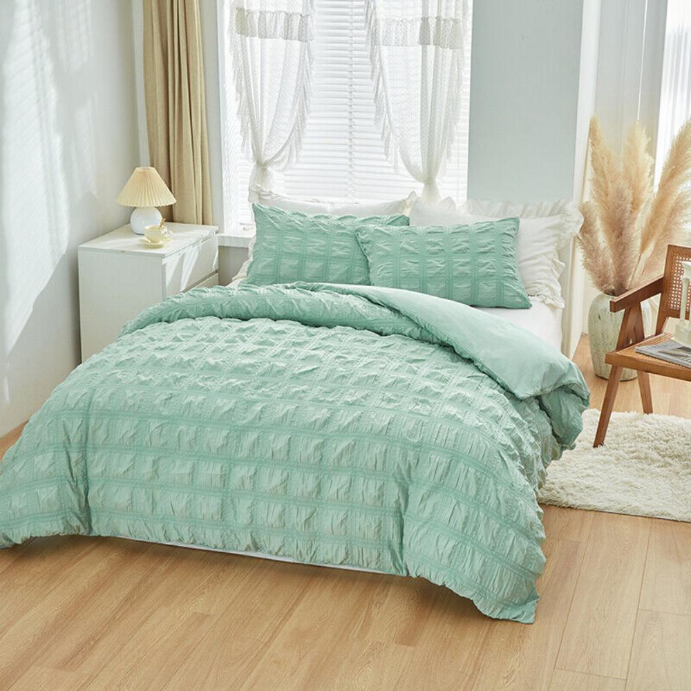 Teal textured comforter set on a bed in a bright bedroom with light wood flooring.