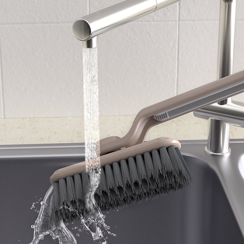 Cleaning brush under running water from a faucet in a kitchen sink.