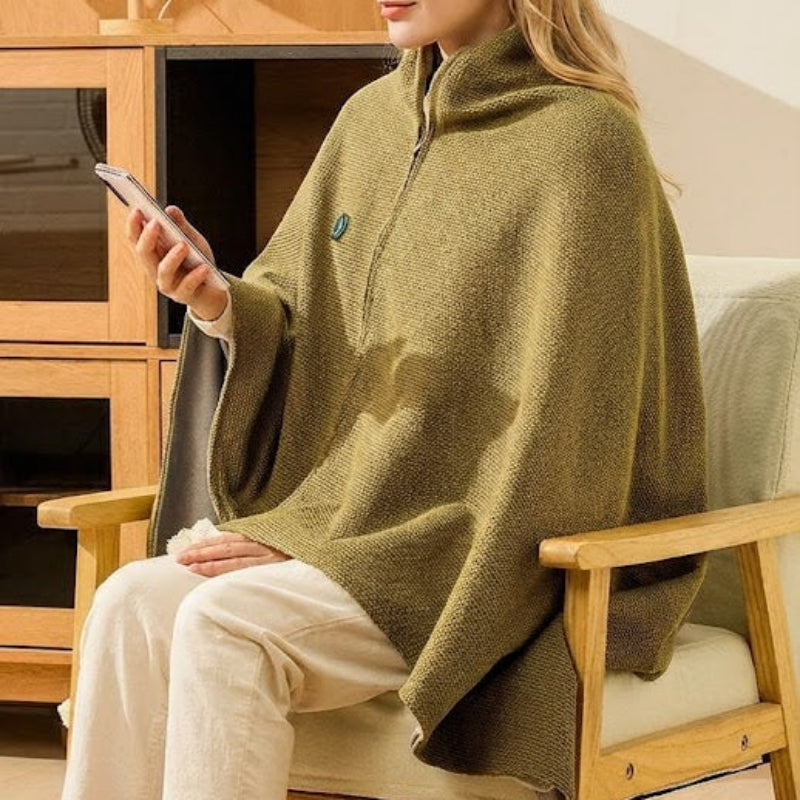 Person wearing a green poncho sitting on a wooden chair indoors.