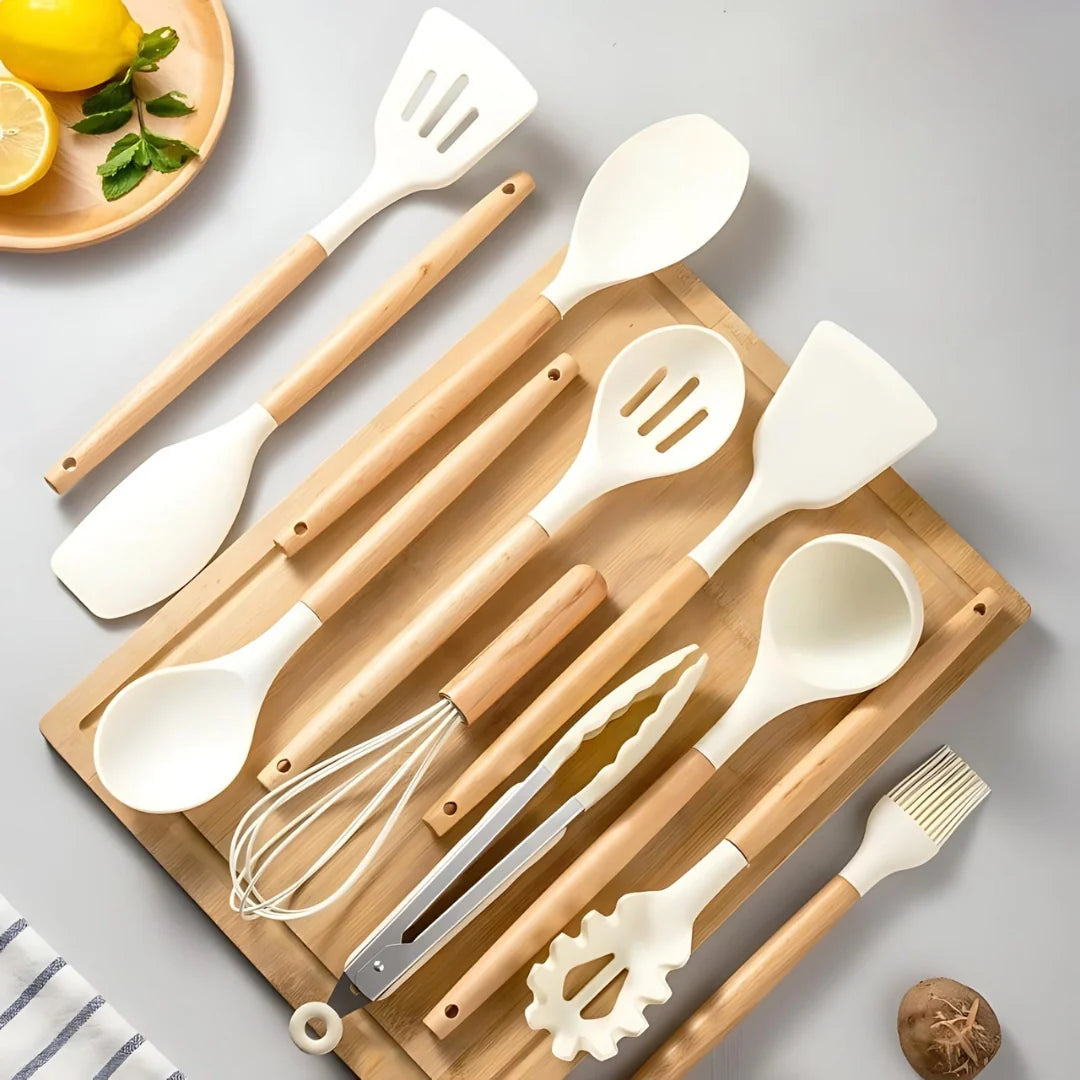 Set of kitchen utensils including spatulas, spoons, and a whisk on a wooden board with a light gray background.