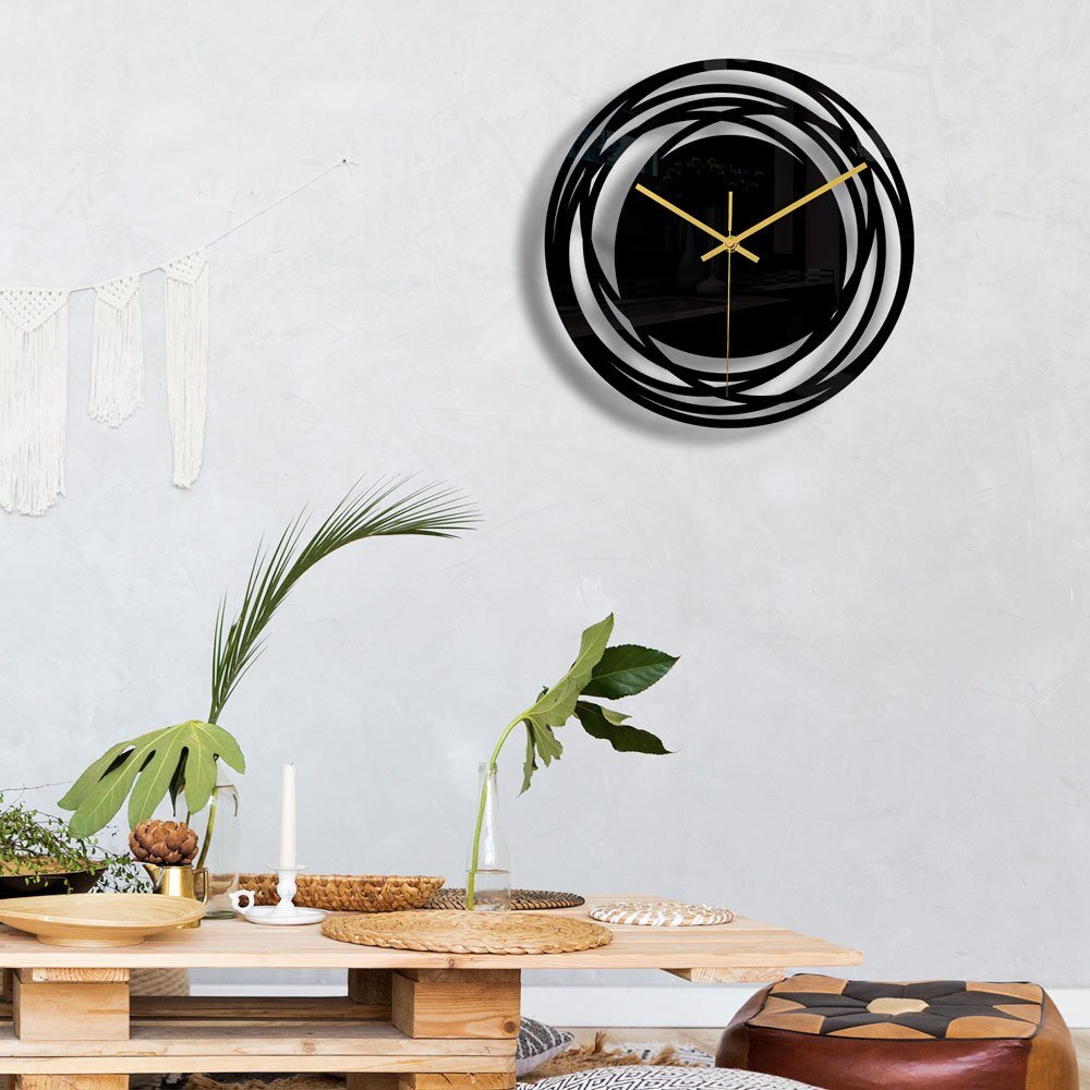 Modern wall clock with black and gold design on a light gray wall above a wooden table.