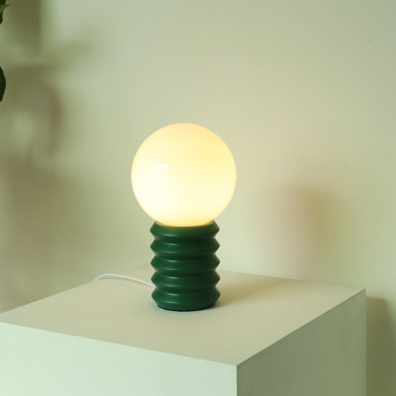 Table lamp with a green base and glowing bulb on a light surface.