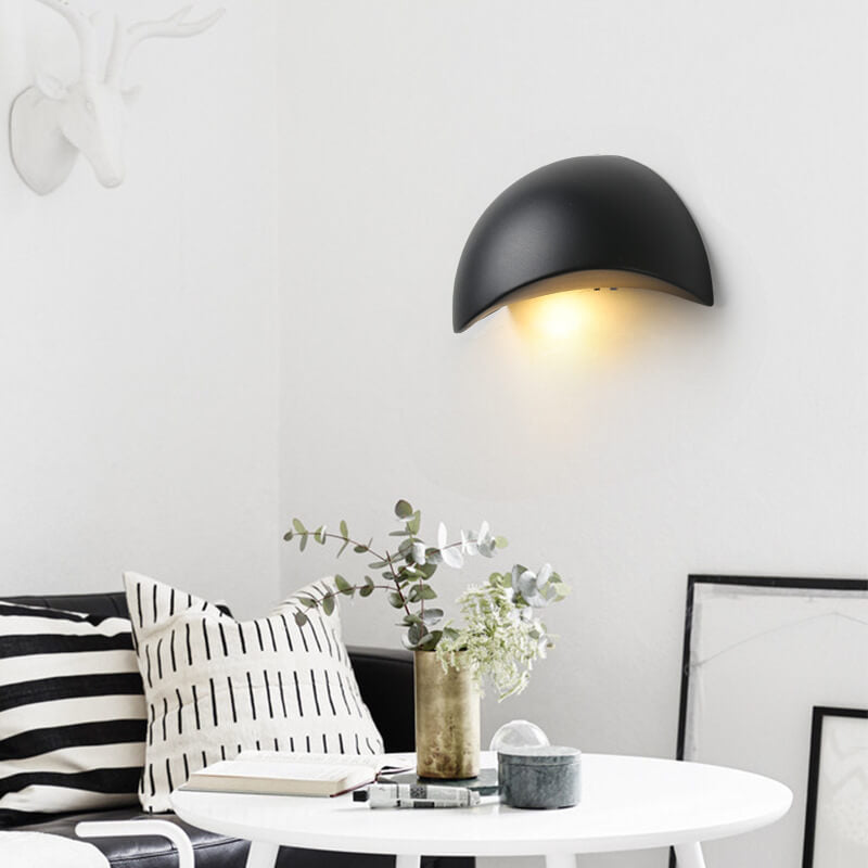 Modern black wall sconce in a living room setting with a table and decorative items.