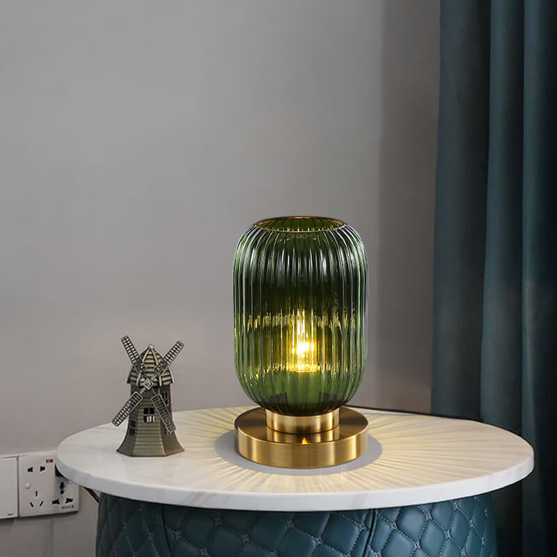 Green glass table lamp with gold base on a round wooden table against a gray wall.