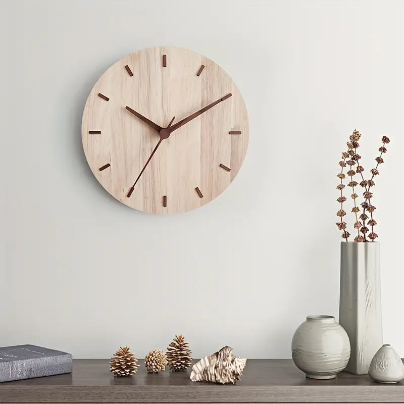 Wooden wall clock on a light gray wall with decorative items on a shelf below.