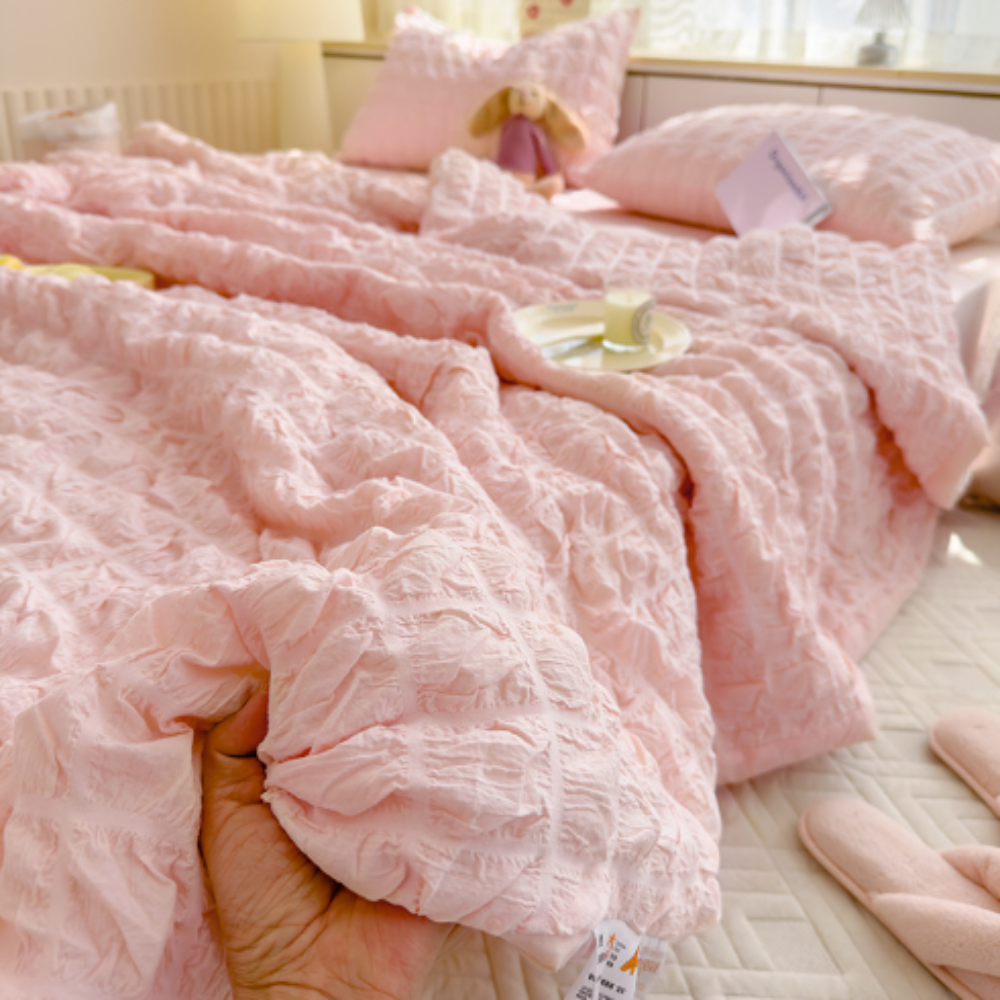 Pink textured comforter on a bed with a blurred background