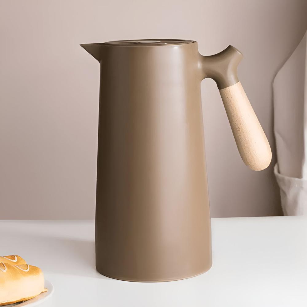 Brown ceramic pitcher with wooden handle on a white surface