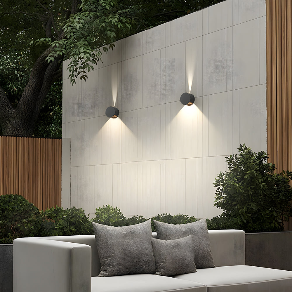Modern outdoor setting with a white sofa, gray cushions, and wall-mounted lights on a tiled wall.