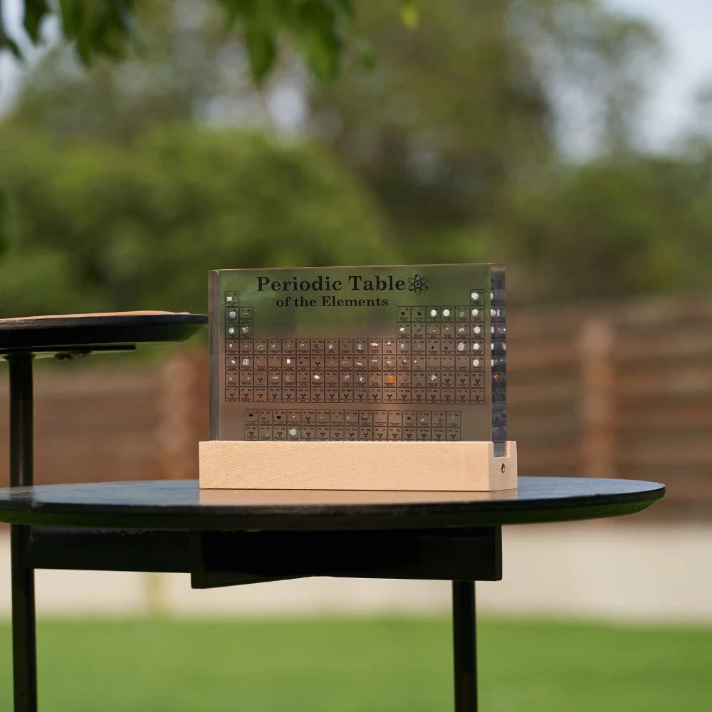 Periodic Table of Elements model on a table outdoors with greenery in the background