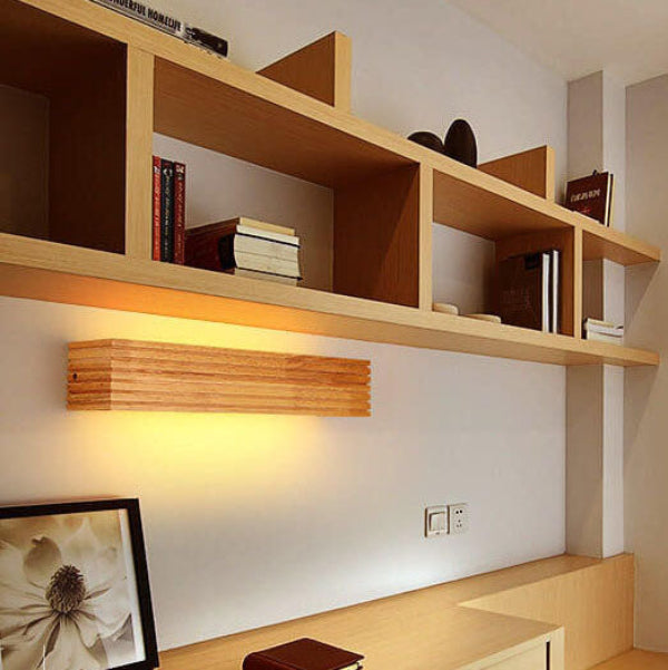 Wooden shelves with books and a light fixture on a white wall.