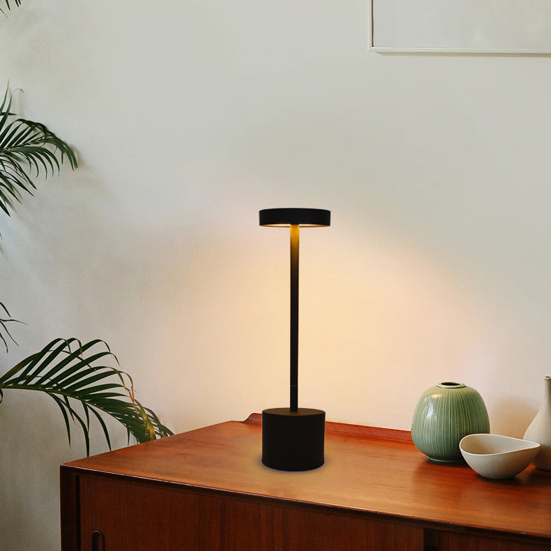 Black table lamp on a wooden surface with a plant and decorative items in the background
