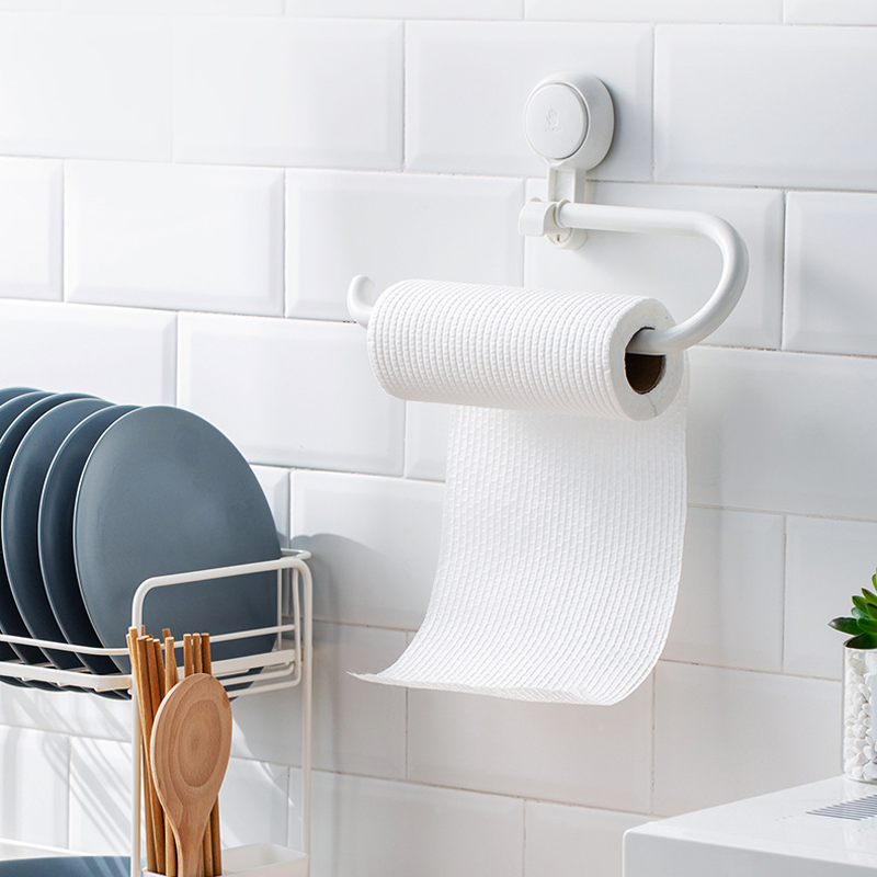 White paper towel holder mounted on a tiled kitchen wall with a roll of paper towels hanging from it.