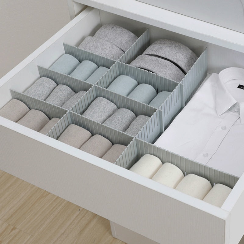 Drawer with organizer containing folded clothes on a light wooden floor.