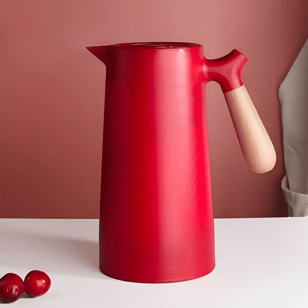 Red pitcher with a wooden handle on a white surface against a pink background