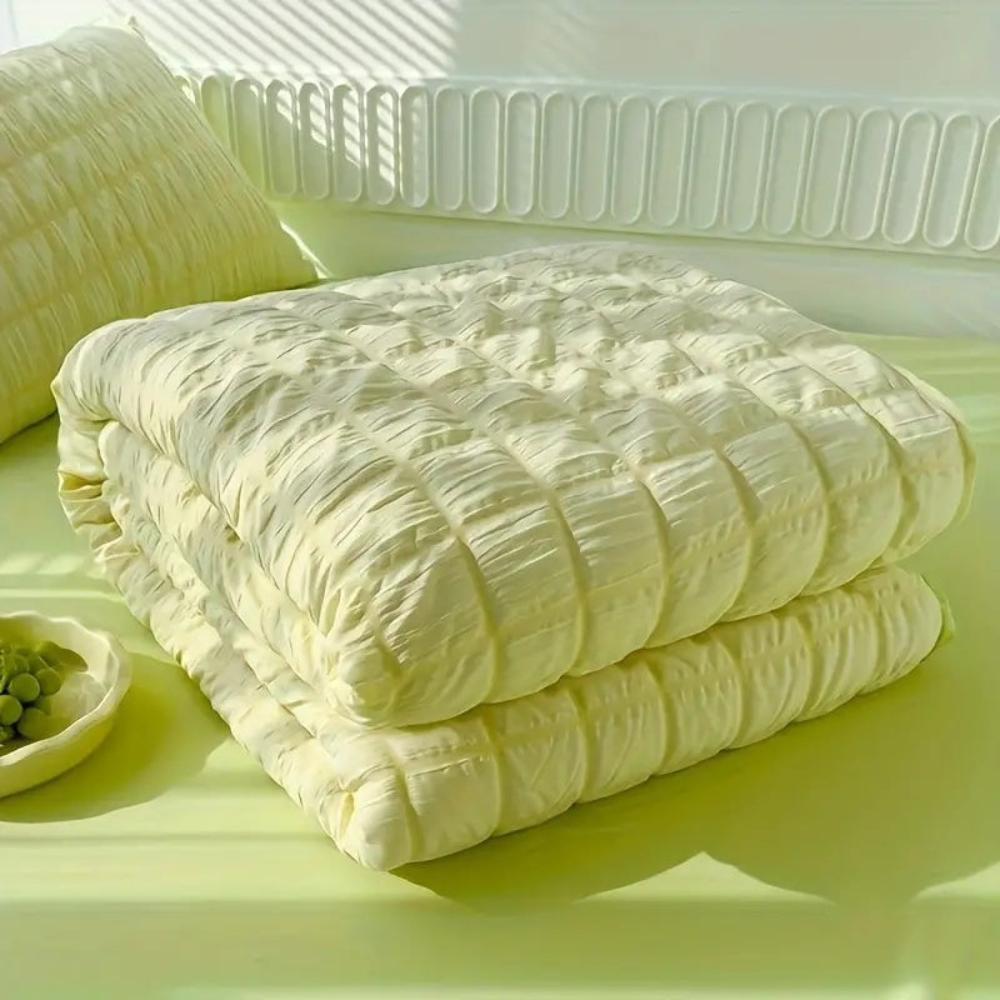 Folded white comforter on a light green surface with a white chair in the background