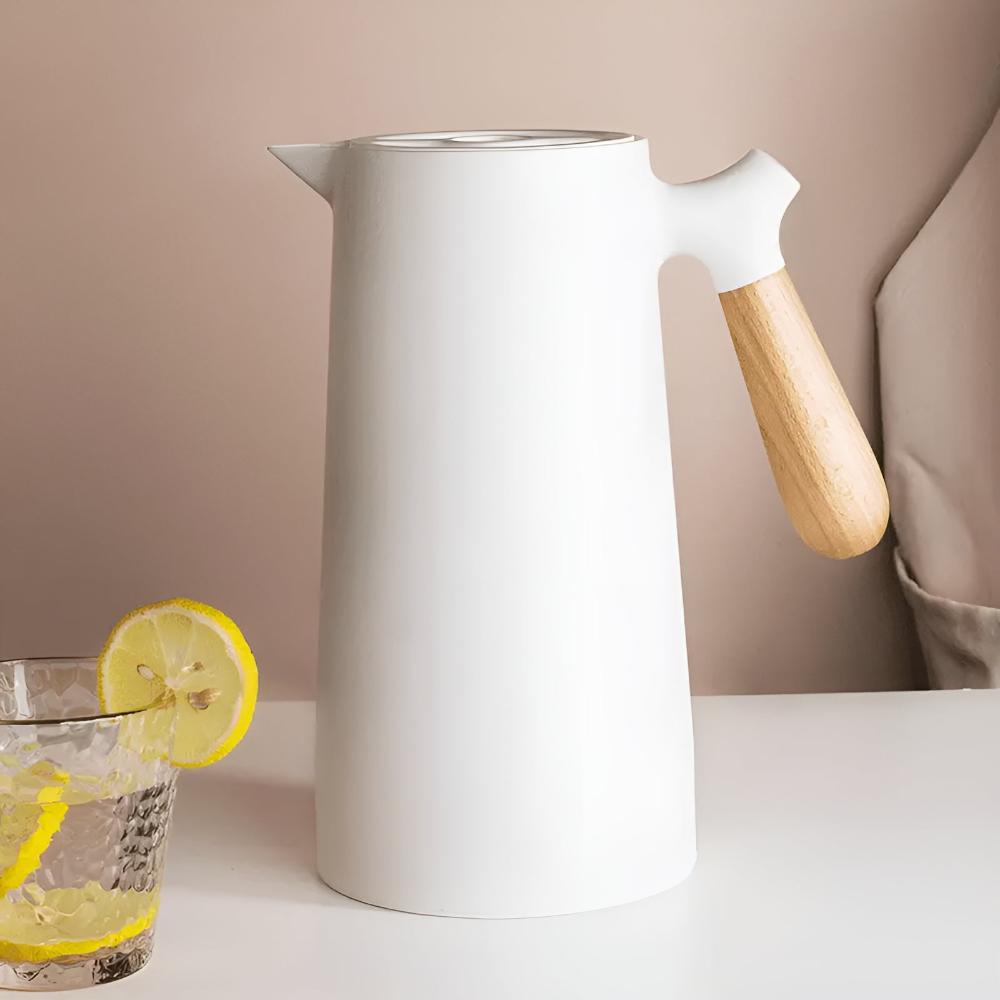 White pitcher with wooden handle next to a glass of lemon water on a neutral background
