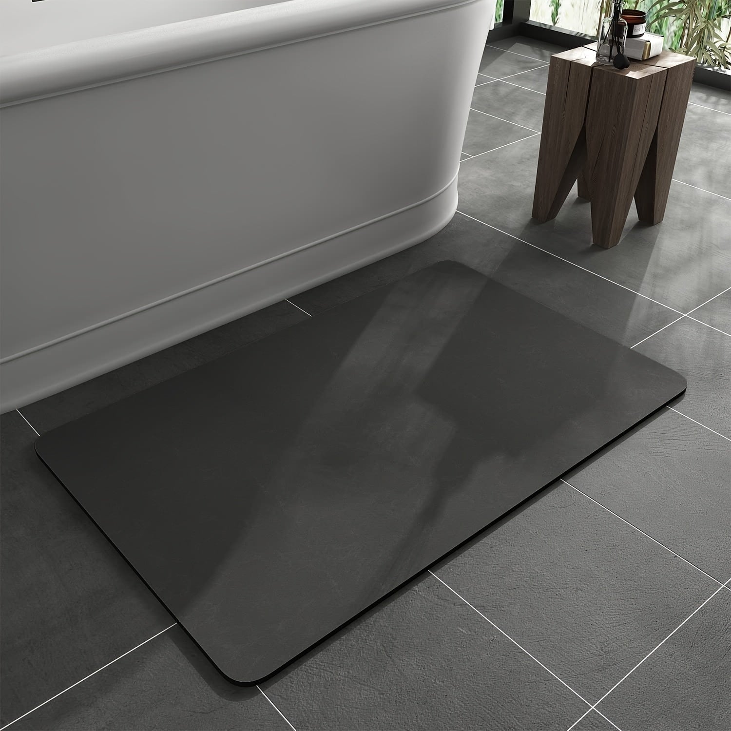 Black bath mat on a tiled bathroom floor next to a bathtub.
