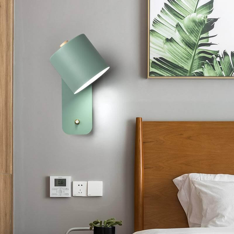 Green wall lamp on a gray wall above a wooden headboard with a plant and decor items.