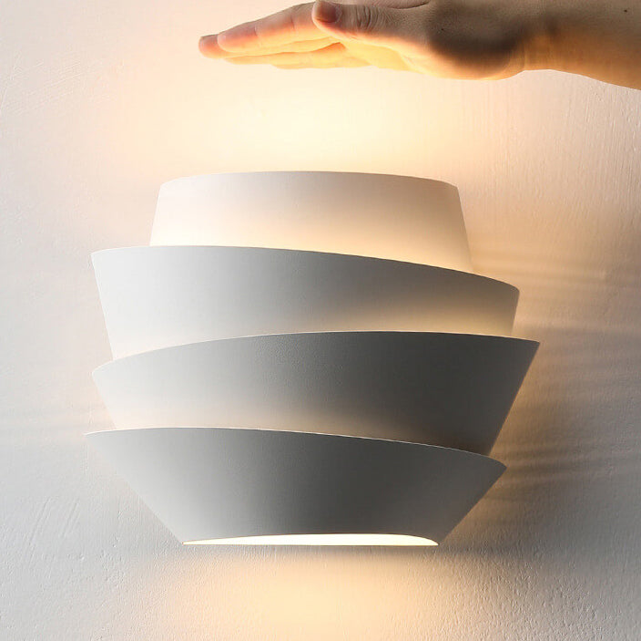 Modern wall-mounted light fixture with a hand reaching towards it on a neutral background
