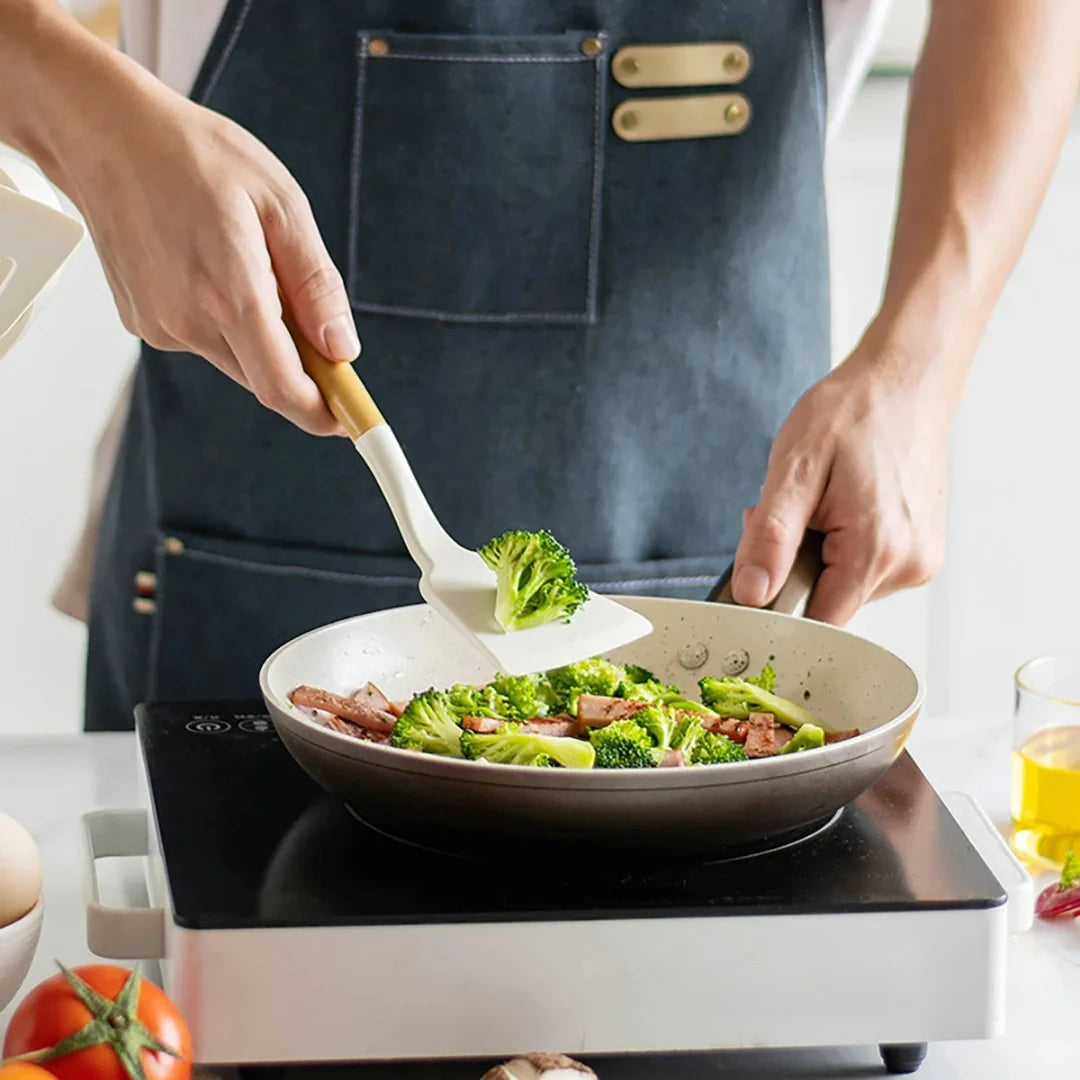 Person cooking vegetables in a pan on a stove, wearing an apron.