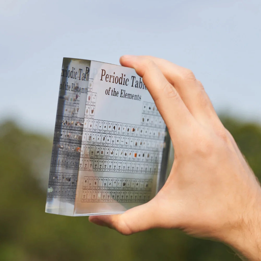 Hand holding a transparent periodic table against a blurred natural background