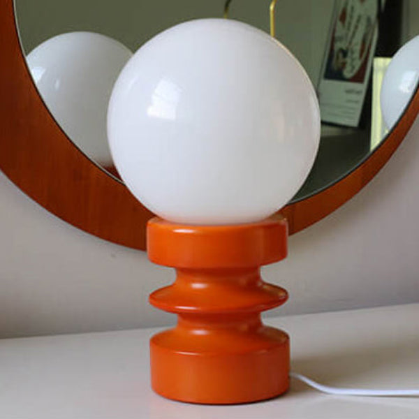 Table lamp with a white globe shade and orange base on a surface.