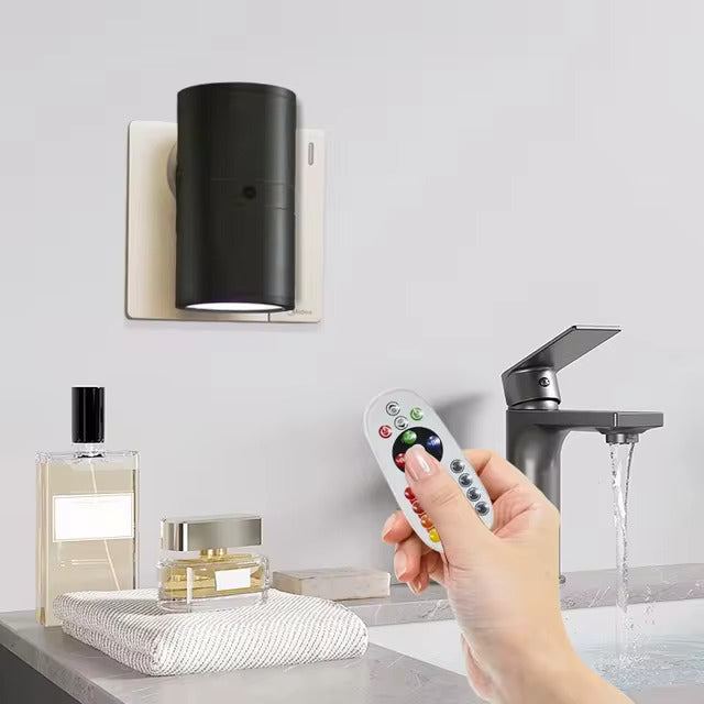 Hand holding a remote control near a sink with a light fixture and perfume bottles in the background.