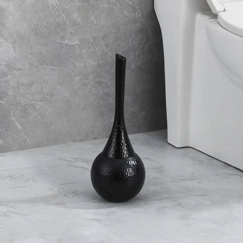 Black toilet brush holder on a bathroom floor next to a toilet.
