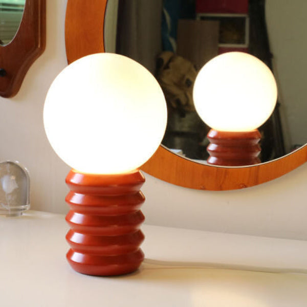 Decorative lamp with a wooden base and spherical glass shade in front of a mirror.
