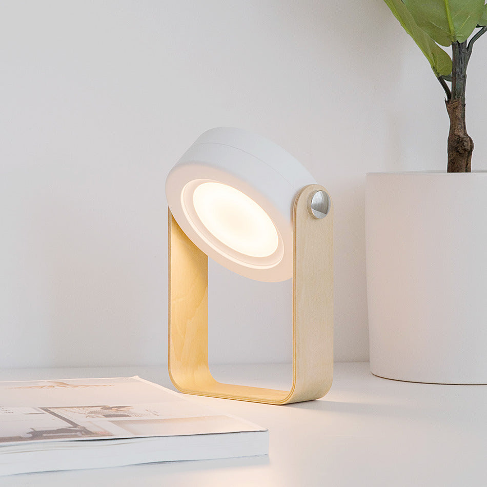 Modern table lamp with a white and gold design on a surface with a plant in the background.