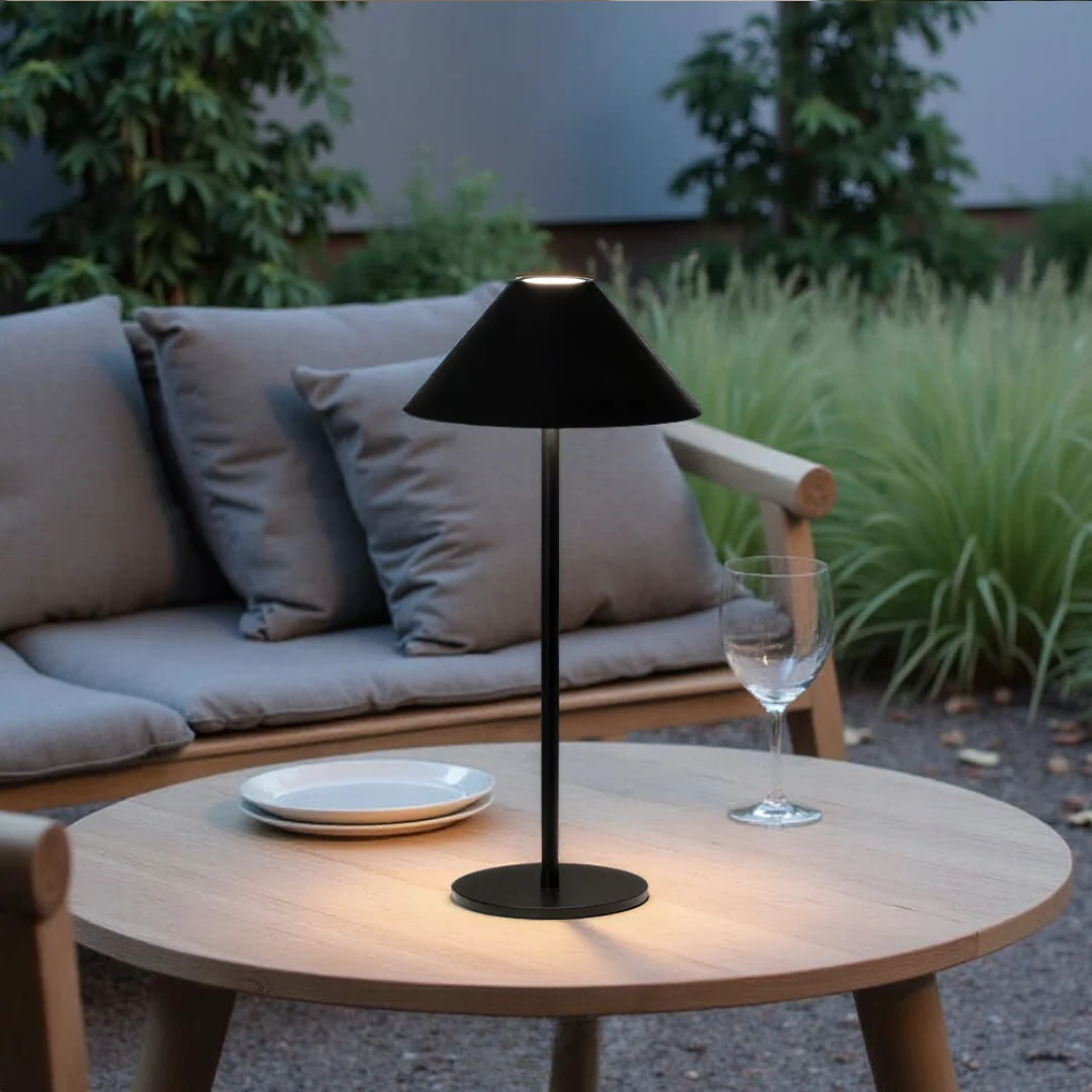 Black outdoor table lamp on a wooden table with a sofa and plants in the background