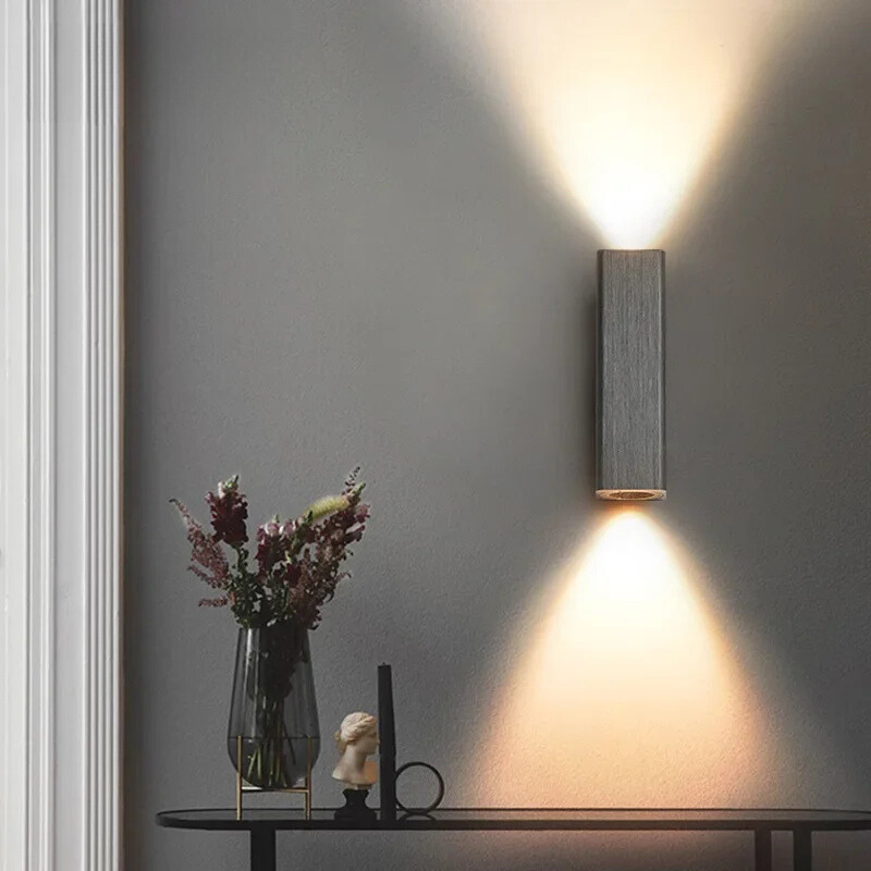 Modern wall light fixture casting a warm glow on a gray wall with decorative items below.