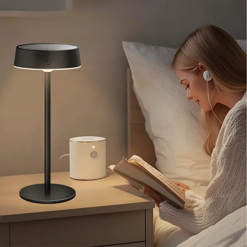 Woman reading a book in bed with a lamp and night light on a bedside table.