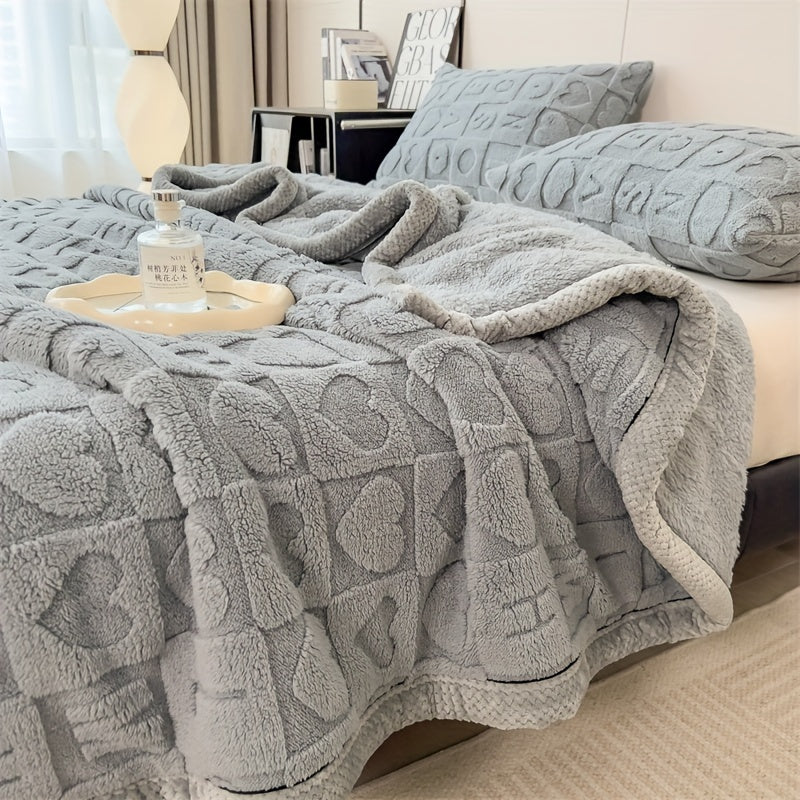 Gray textured blanket draped over a bed with pillows and a small table.