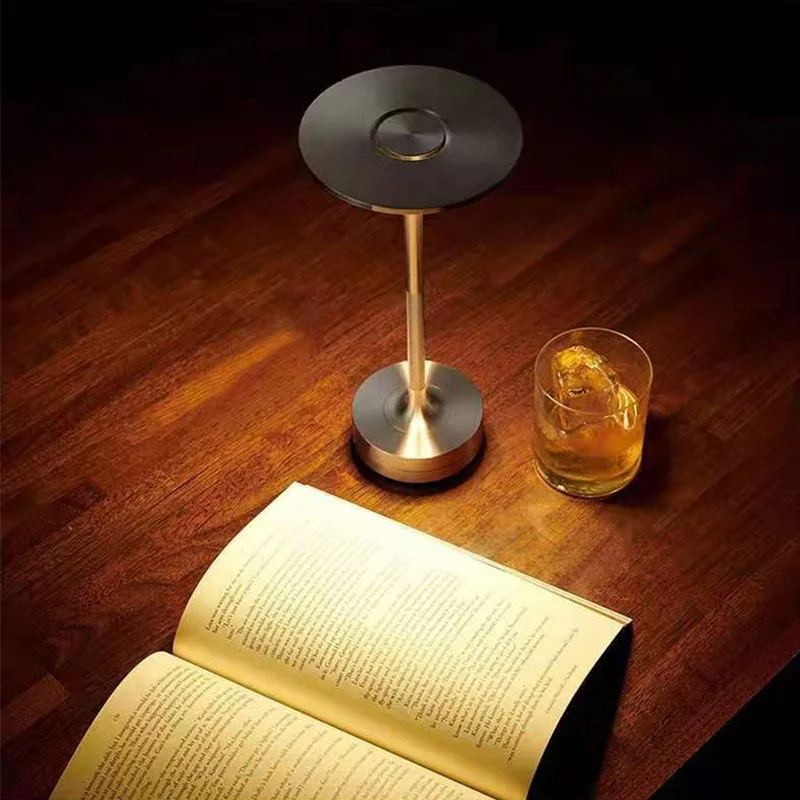 Small lamp on a wooden table with an open book and a glass of liquid.