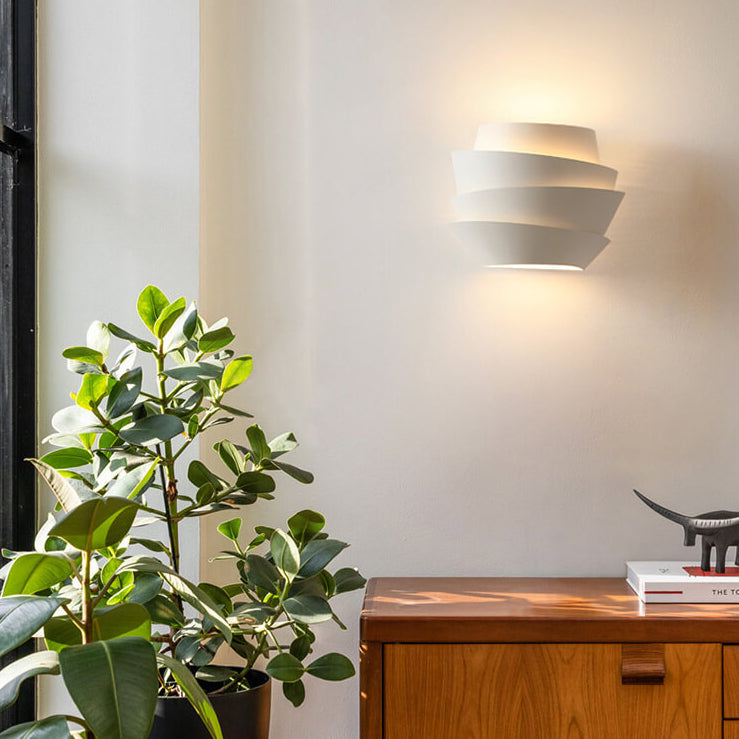Modern wall light fixture on a white wall with a plant and wooden cabinet in the foreground.