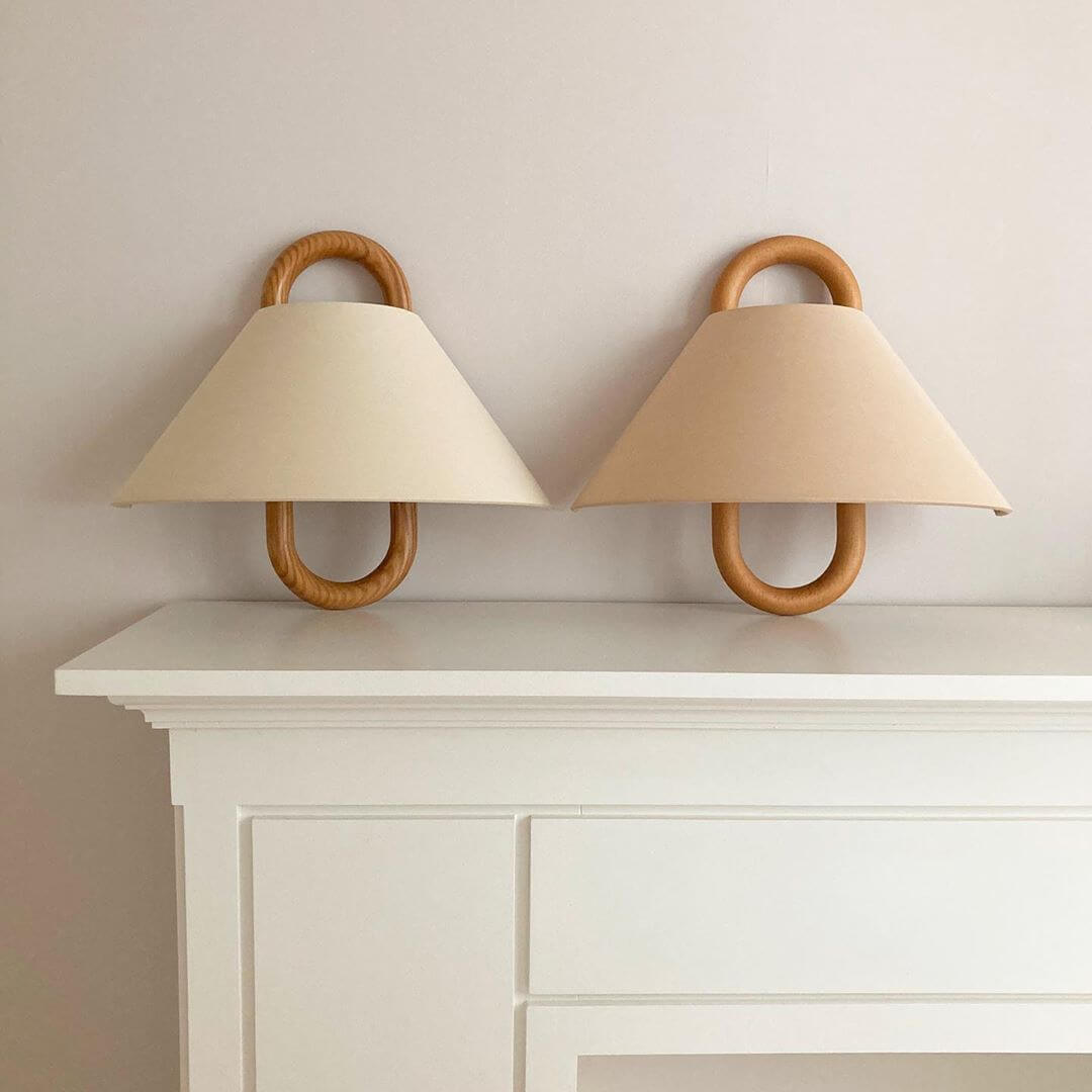 Two wall-mounted lamps with wooden handles and beige lampshades on a white shelf against a light gray wall.