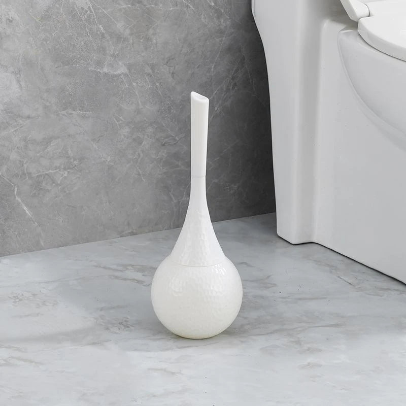 White toilet brush holder on a bathroom floor next to a toilet.