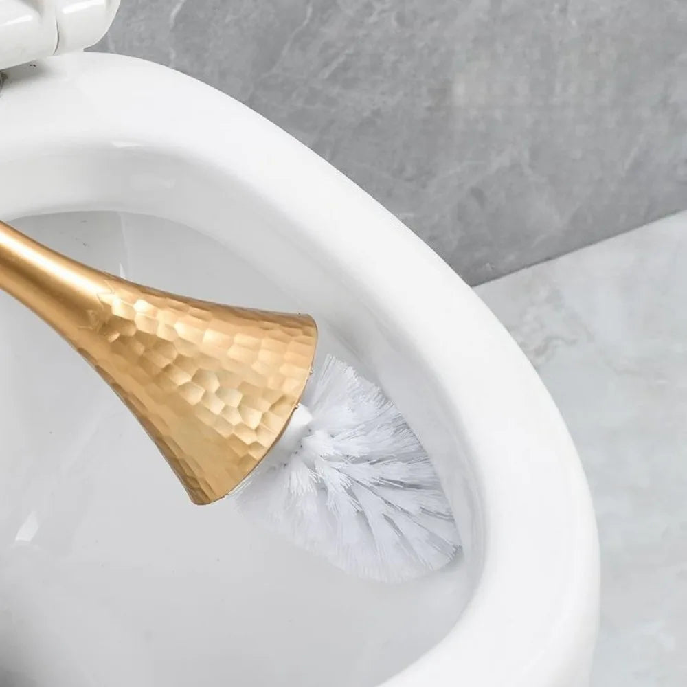 Gold toilet brush with white bristles inside a white toilet bowl against a gray marble background