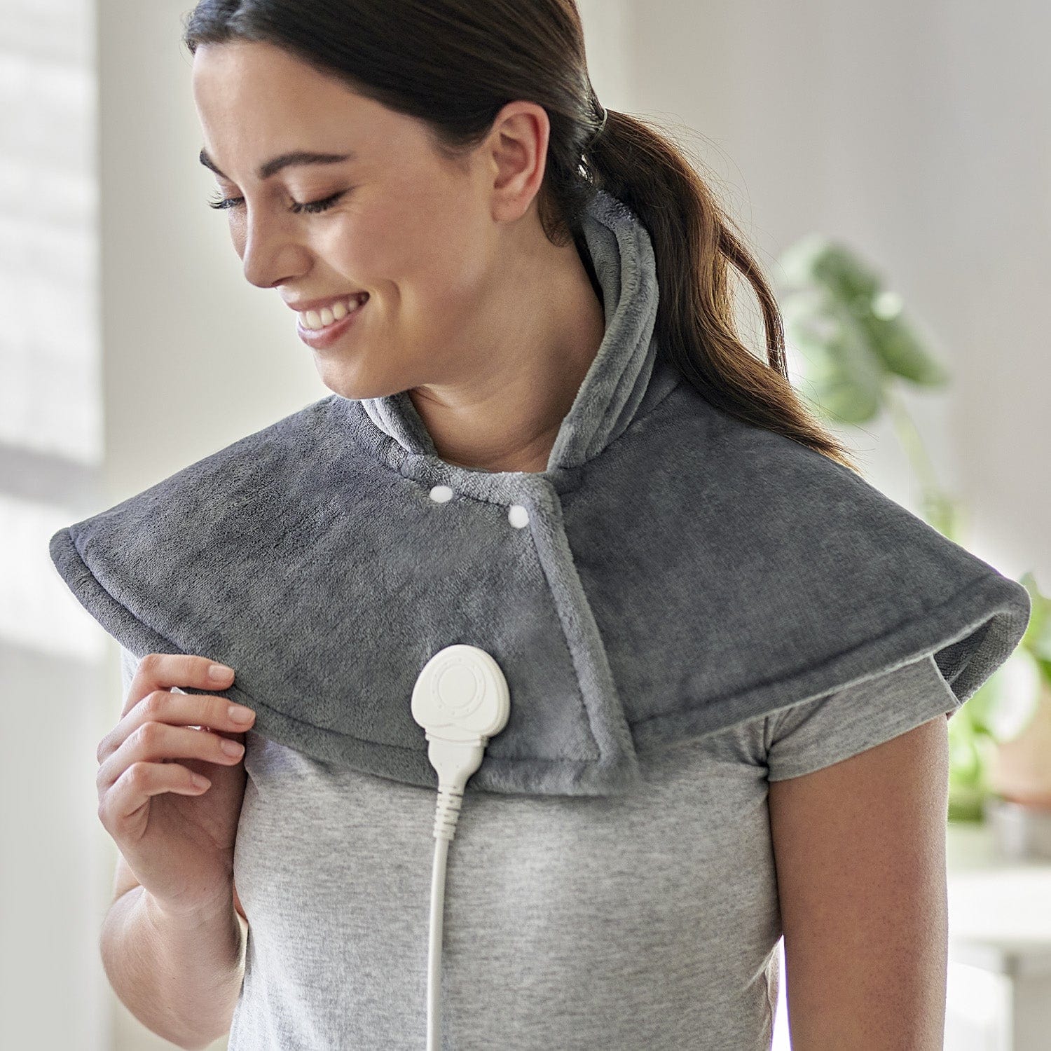 Woman wearing a gray neck and shoulder massager in a home setting