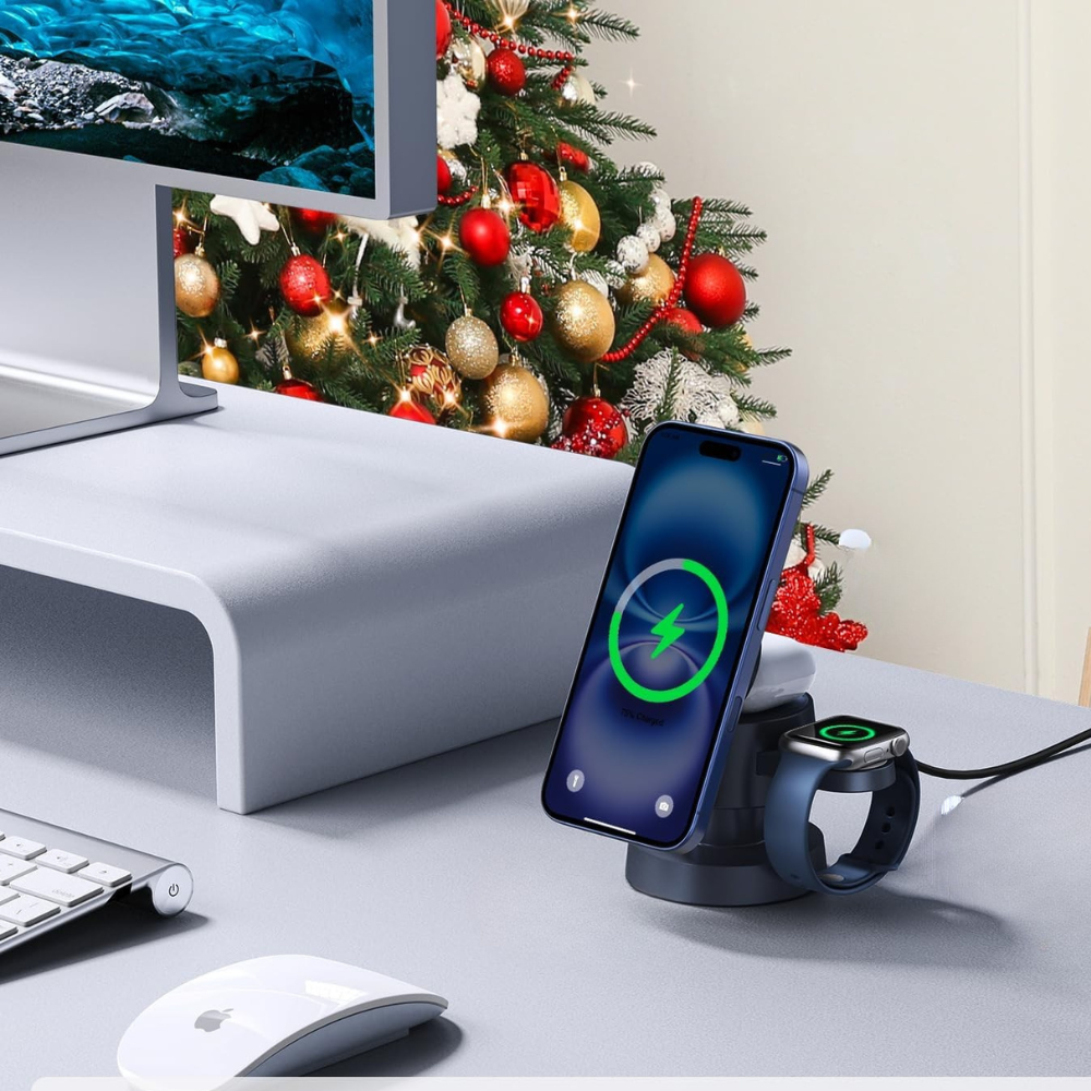 Wireless charging station on a desk with a phone, watch, and computer monitor in front of a Christmas tree.