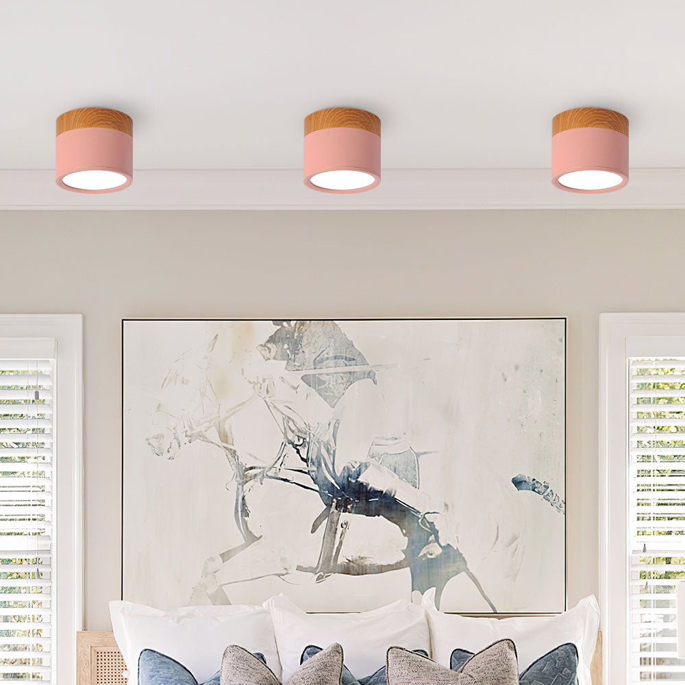 Three ceiling lights with pink shades in a room with abstract art and pillows.
