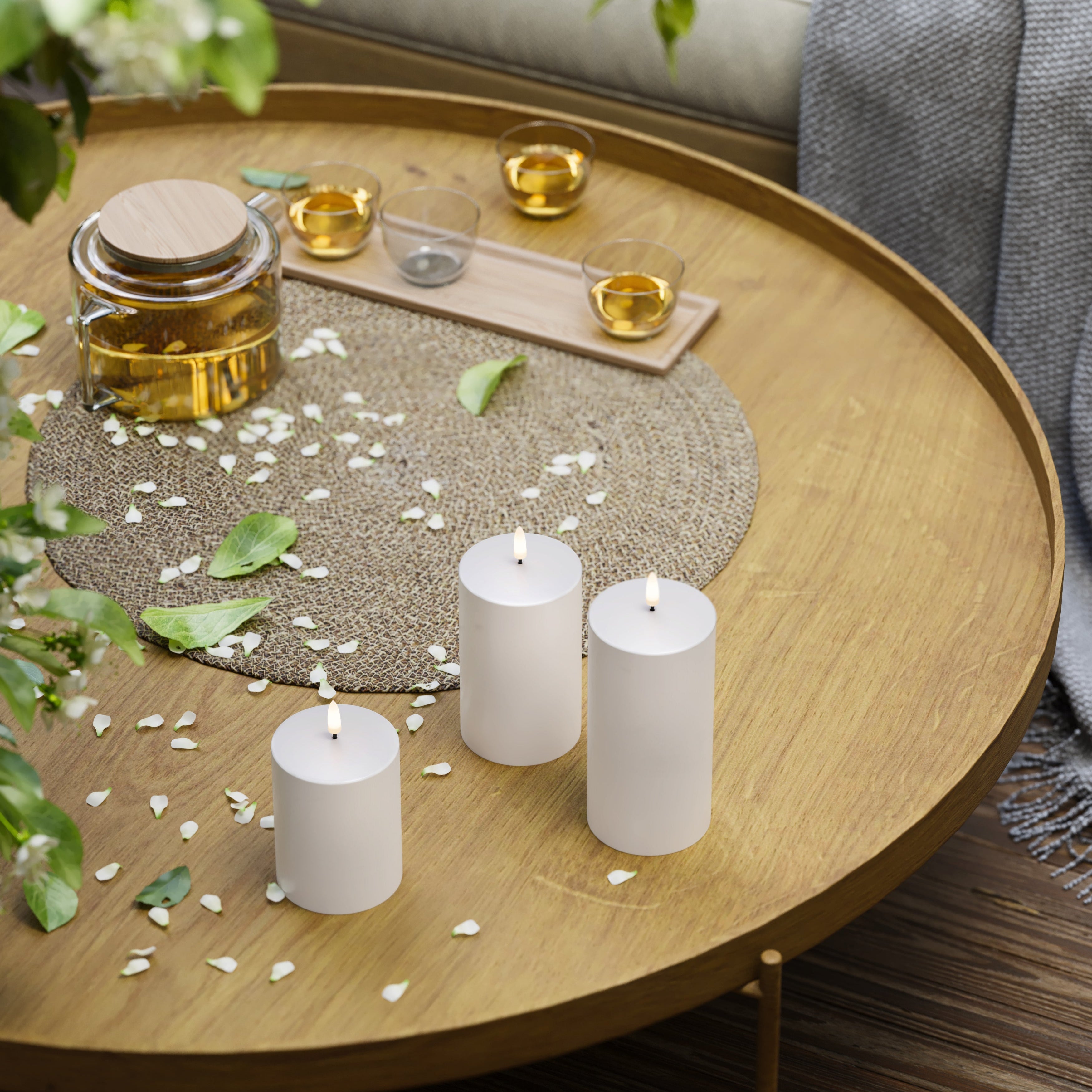 Round wooden table with white candles, small jars, and greenery in a cozy indoor setting.