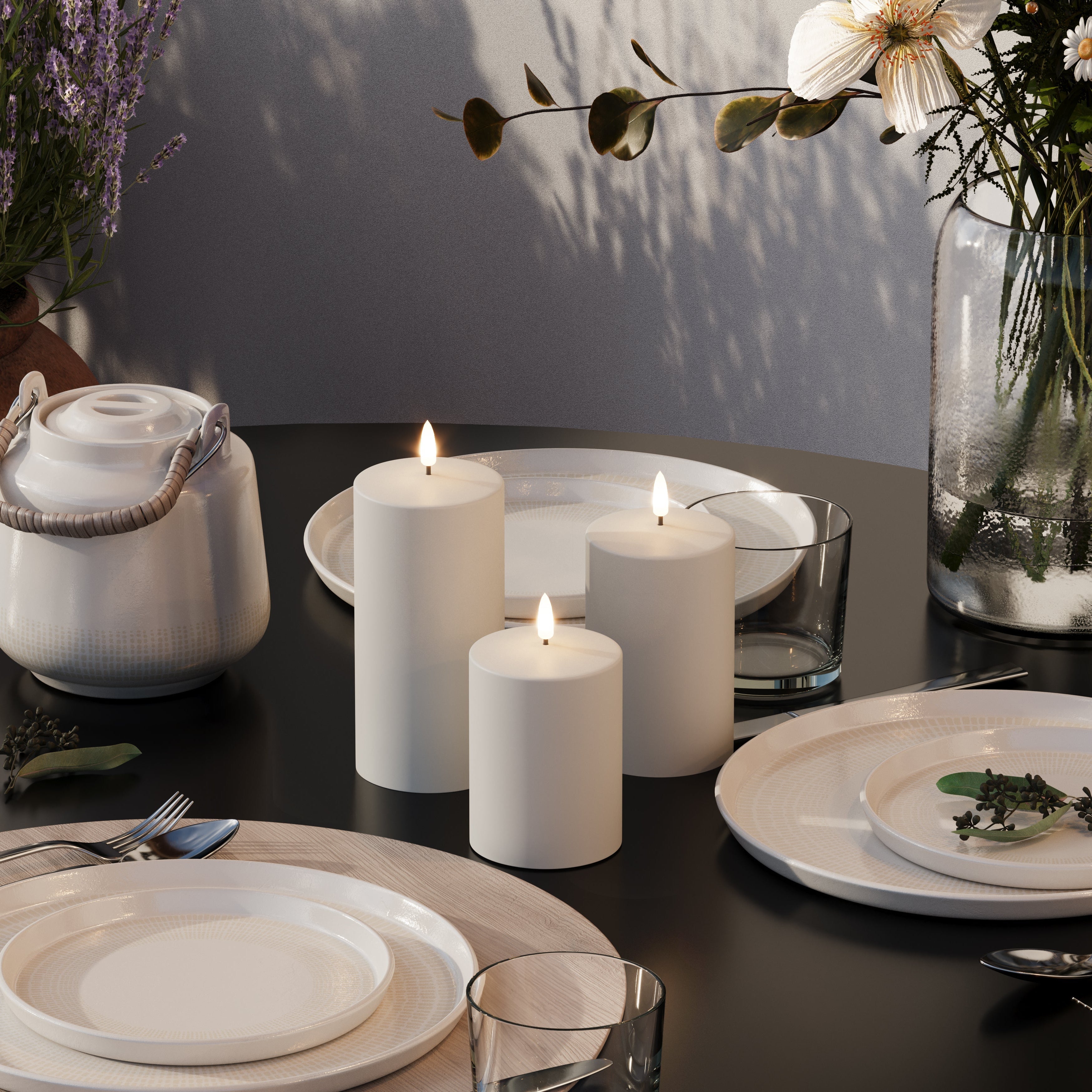 Dining table setting with white candles, plates, and a teapot.